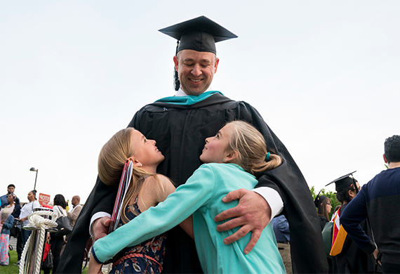 a的图像n adult graduate hugging two children.